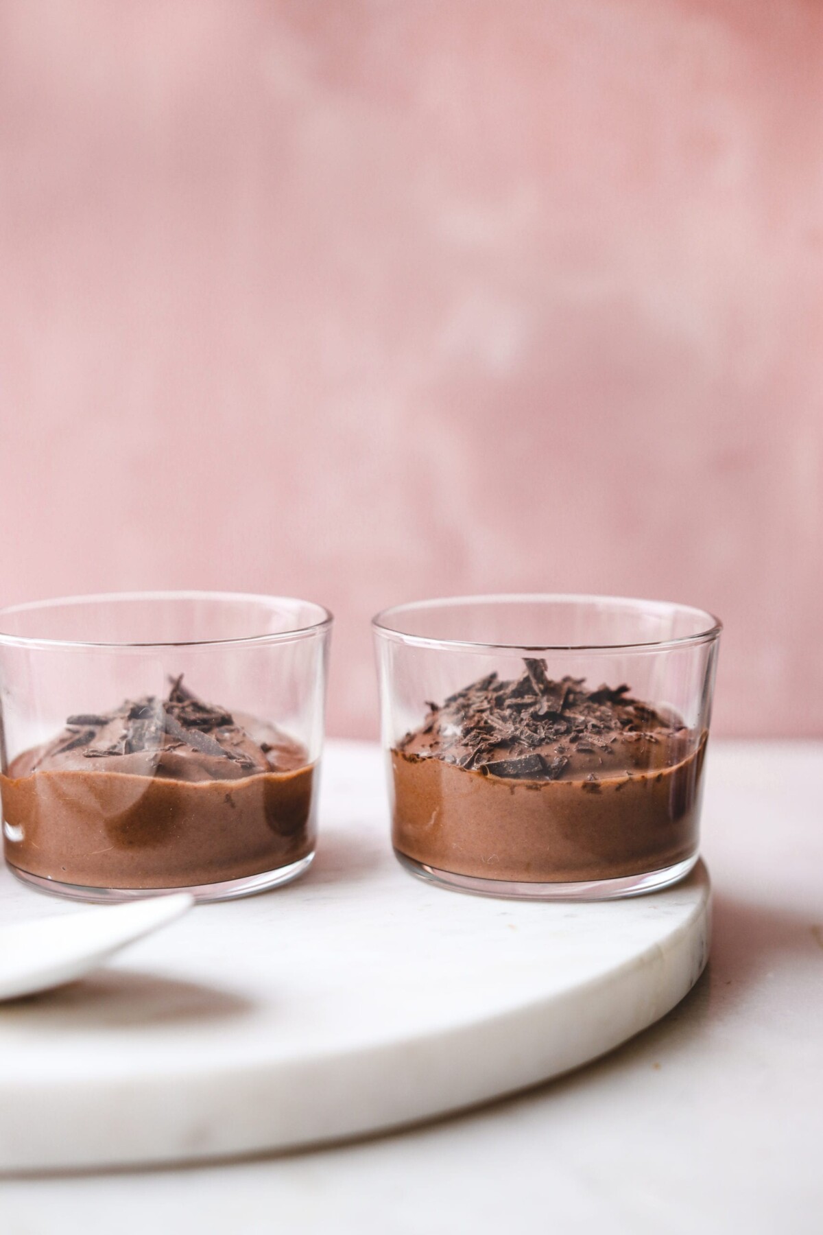 two glasses of vegan chocolate mousse on a white surface