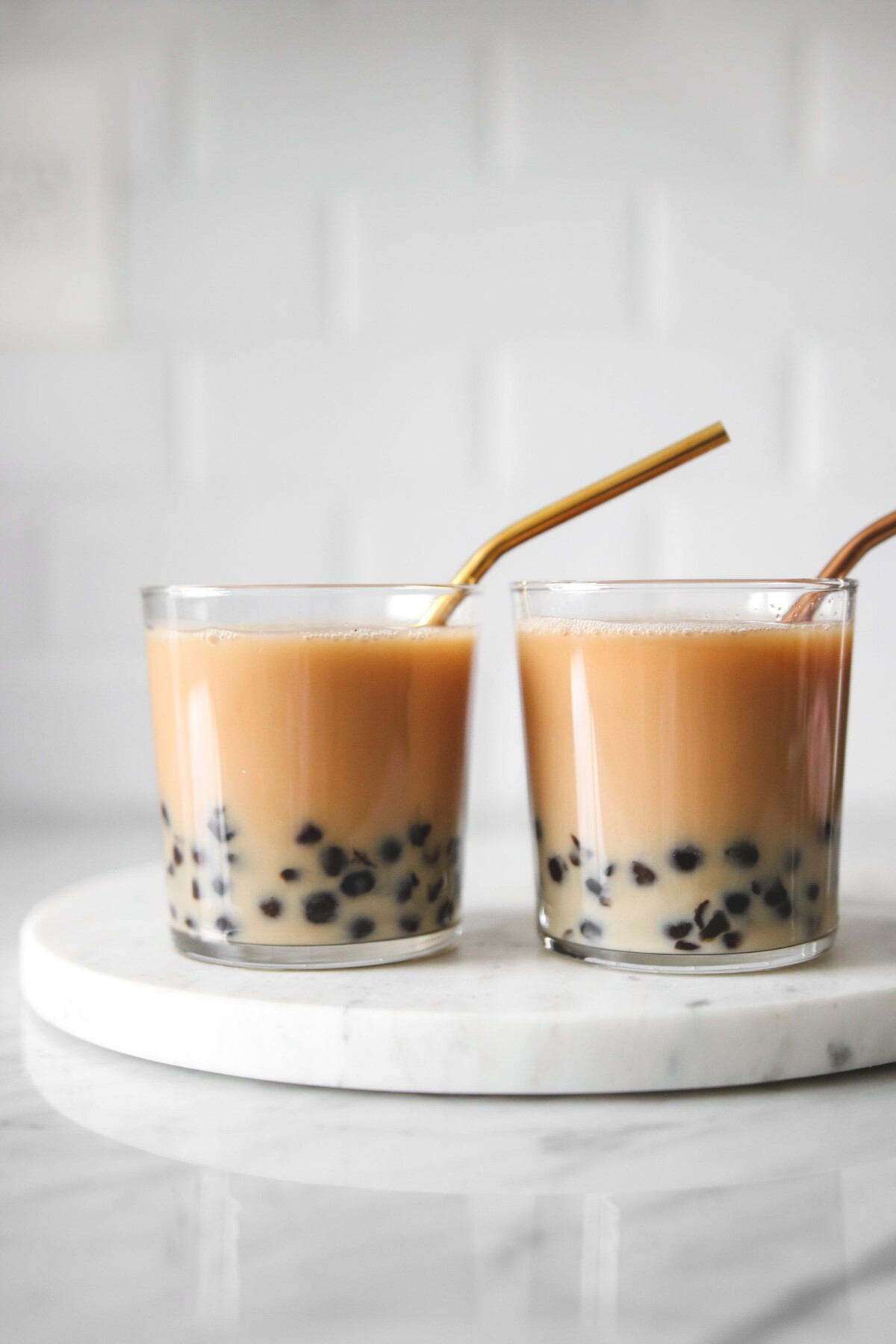 a closeup of two glasses filled with this bubble tea recipe and tapioca pearls. 