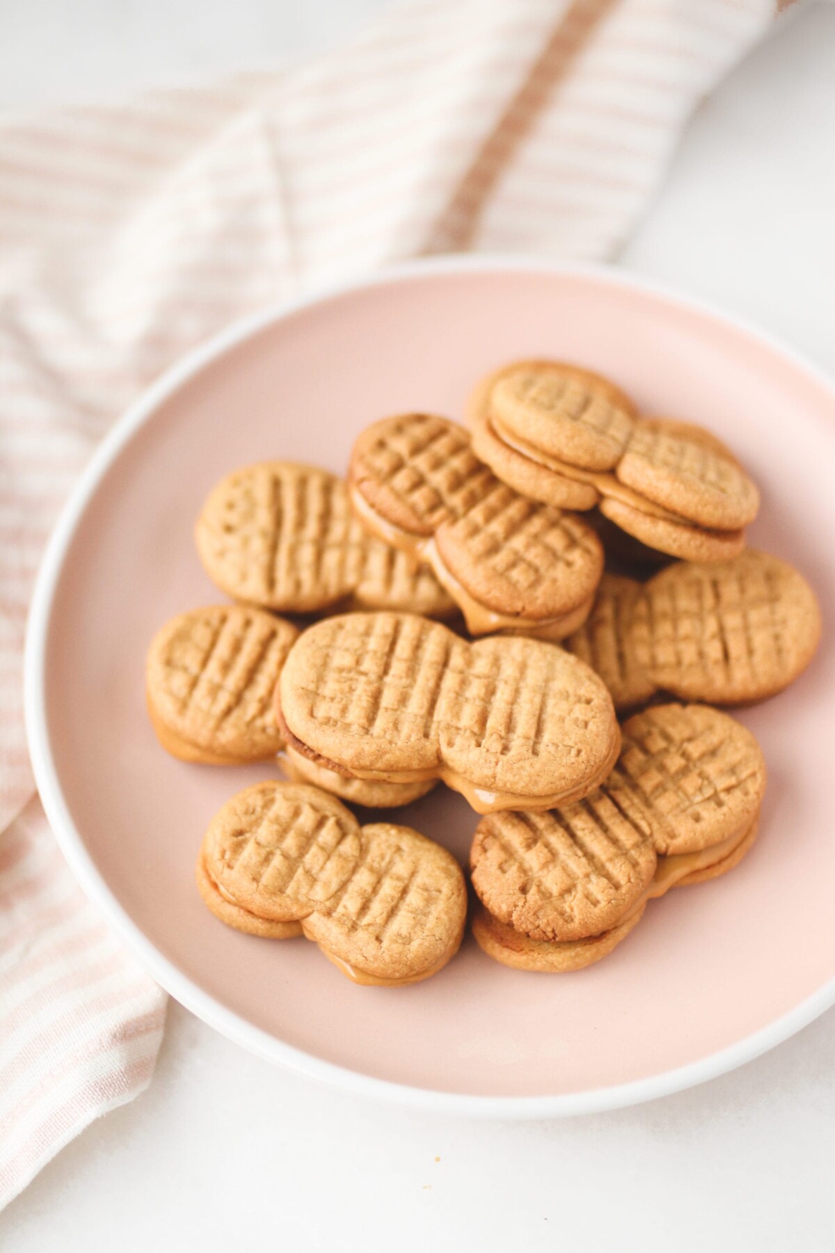 a close up of peanut butter sandwich cookies stacked on a pink plate