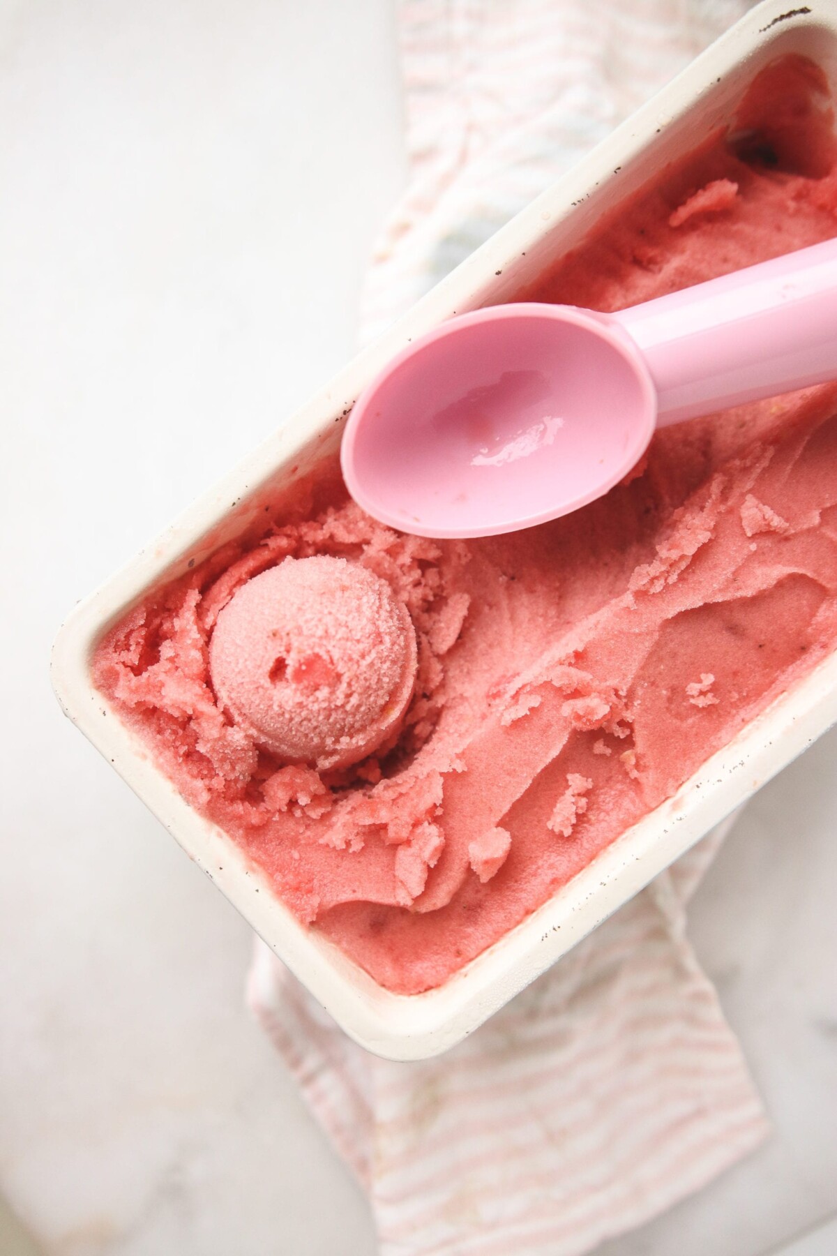 a pink ice cream scoop resting on top of watermelon sugar free sorbet. 