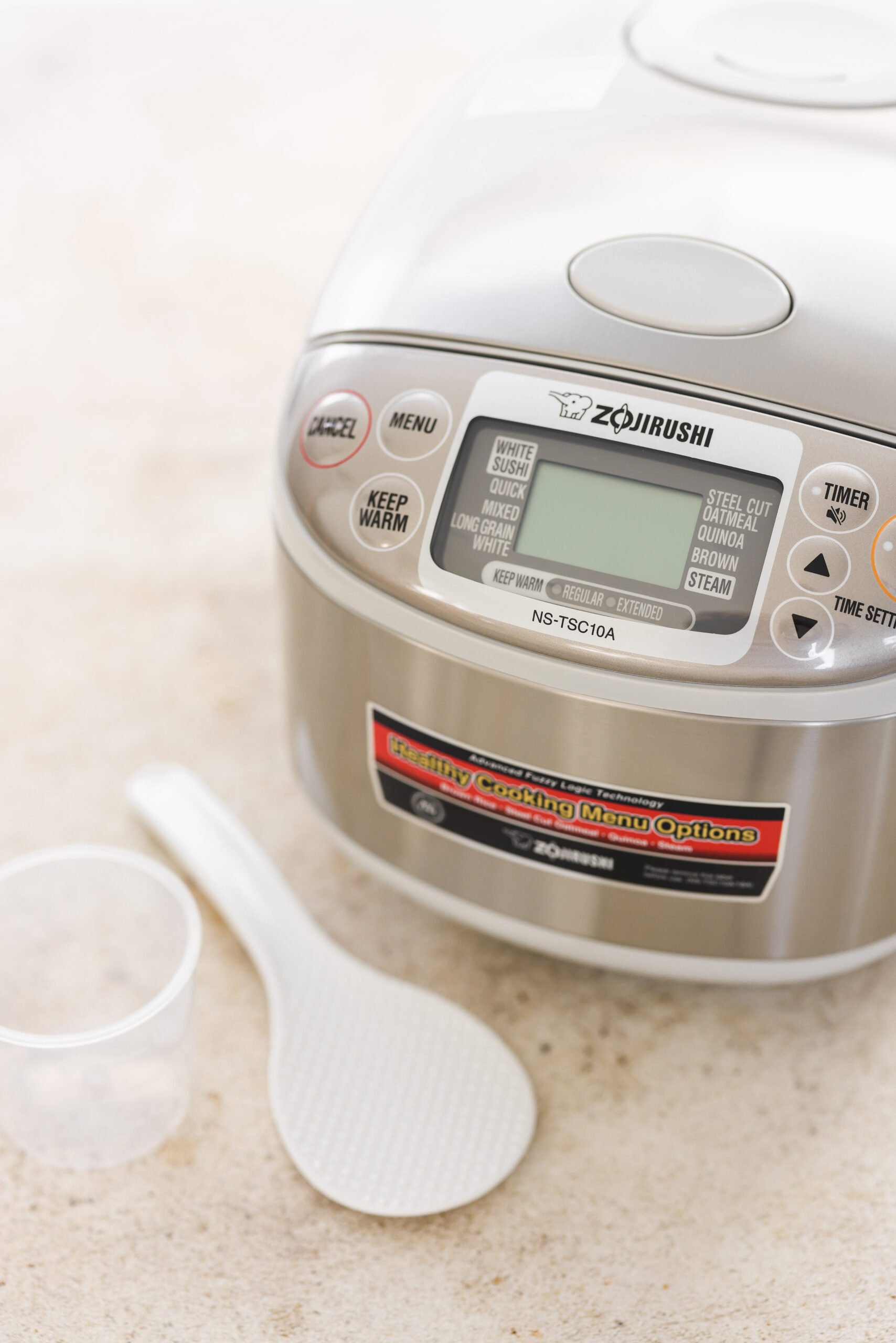 a silver rice cooker next to a measuring cup and rice spoon