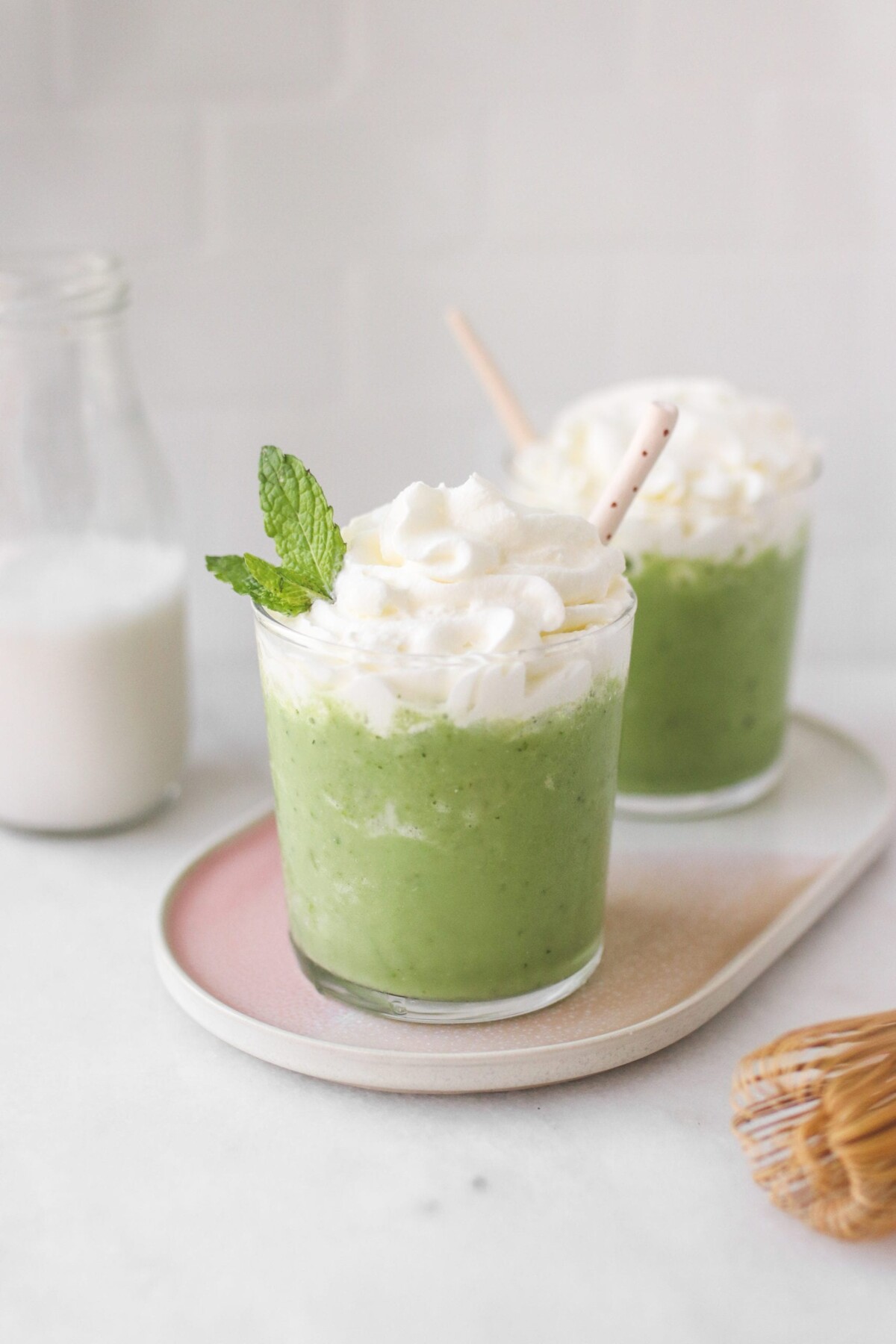 two glasses filled with vegan matcha frappe and topped with whipped cream and straws