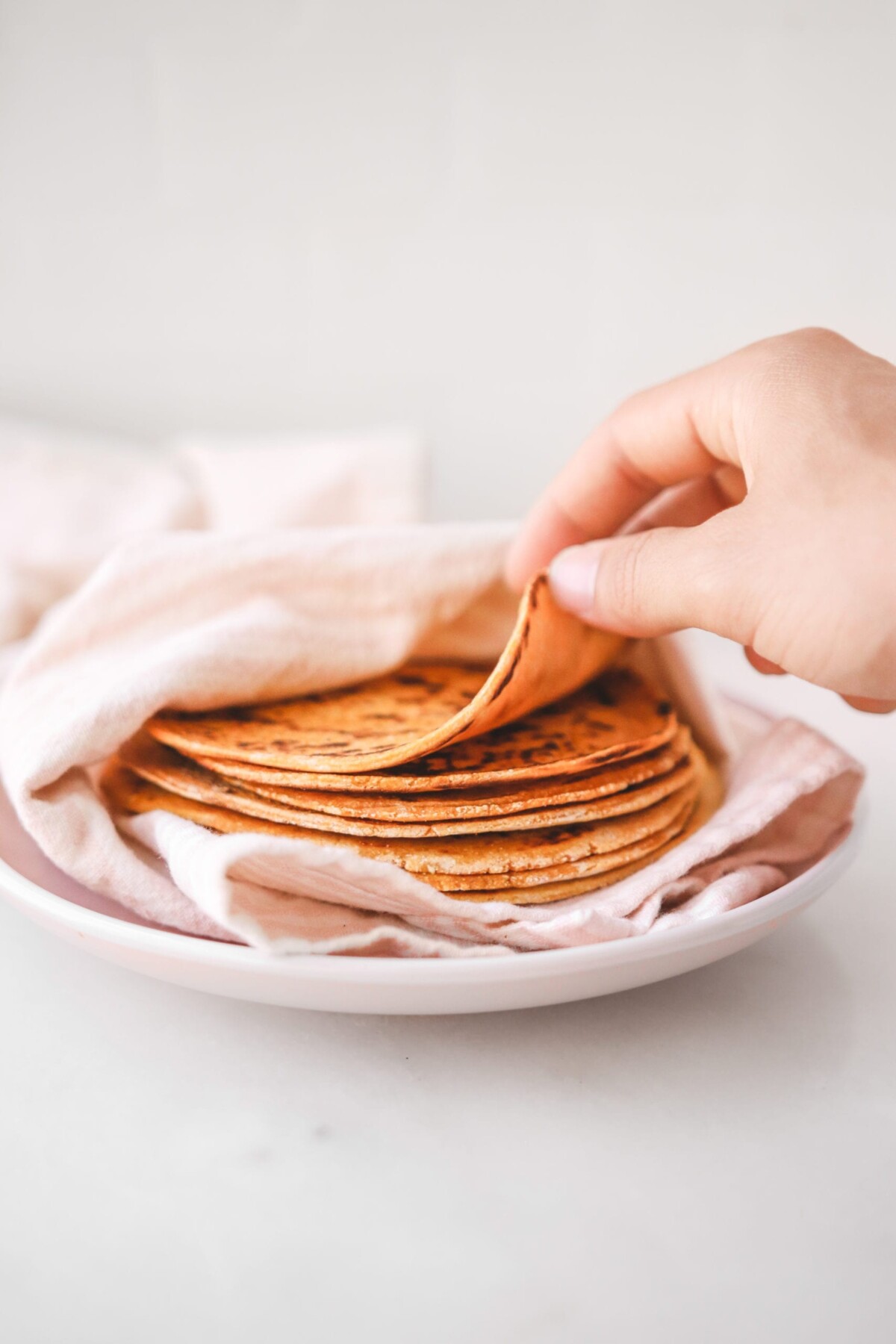 a hand picking up a sweet potato tortilla from a stack of tortillas