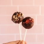 a hand holding two chocolate coated cake balls on lollipop sticks