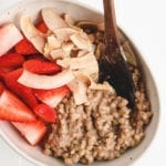 a bowl of buckwheat porridge topped with coconut flakes and fresh strawberries.