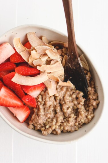 a bowl of buckwheat porridge topped with coconut flakes and fresh strawberries.