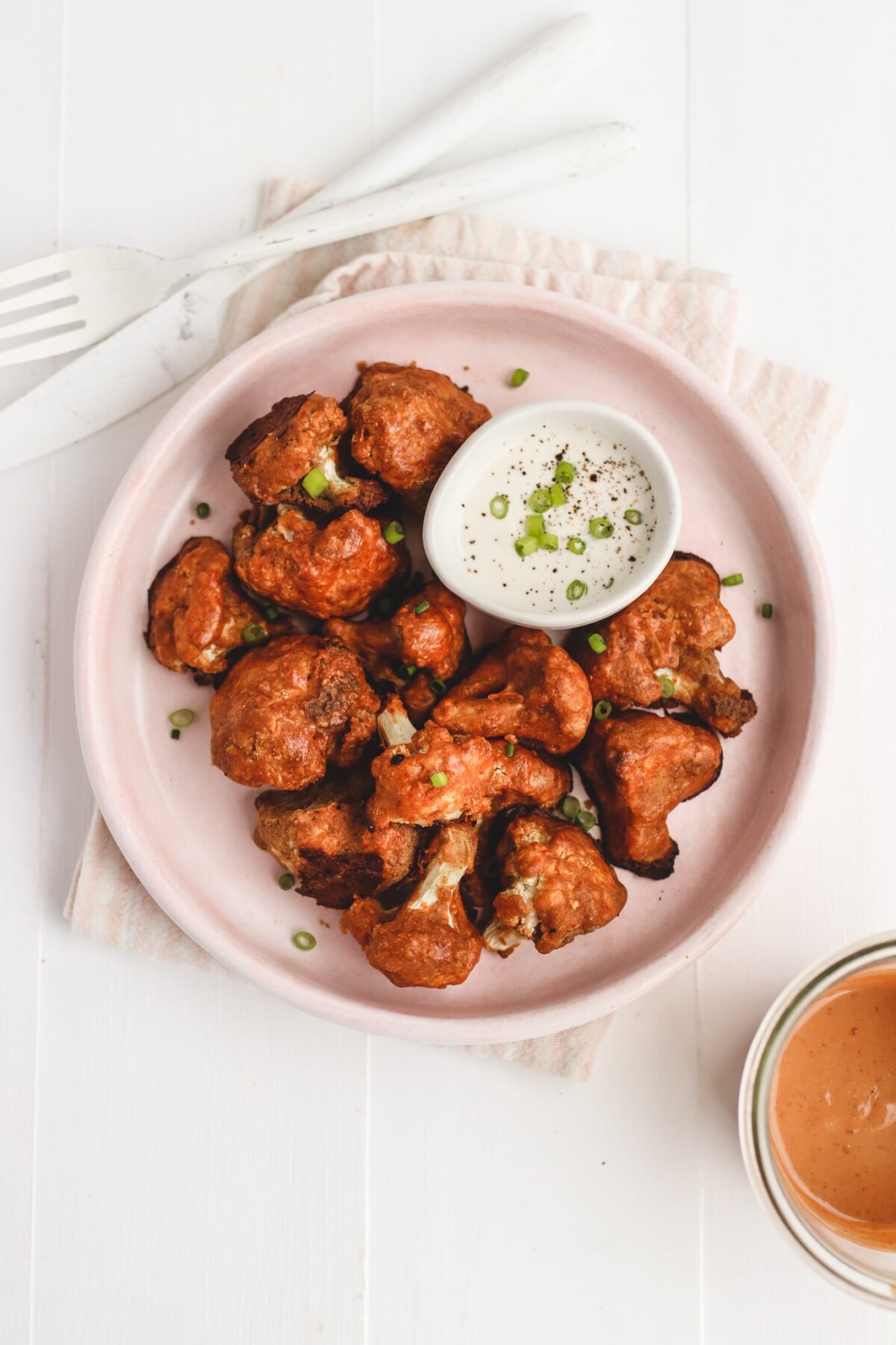 an overhead shot of cauliflower buffalo wings on a pink plate text to a small bowl of dipping sauce