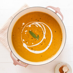 a bowl of pumpkin lentil soup topped with vegan cream and black pepper