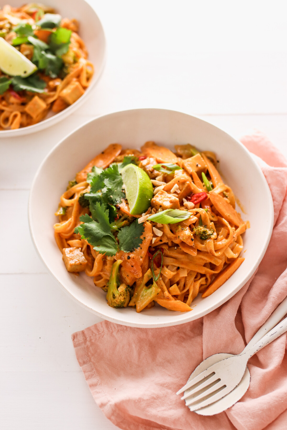 two bowls of red curry noodles topped with cilantro and lime wedges