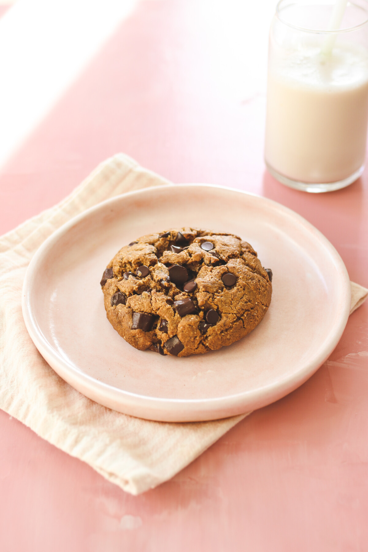a chocolate chip cookie on a pink plate next to a glass of milk. 