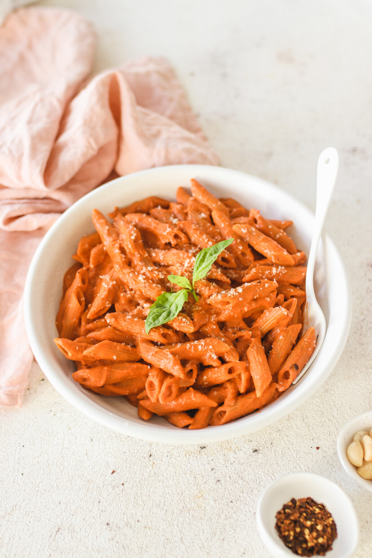 a white bowl filled with vegan vodka alla penne with a spoon resting on the side. 