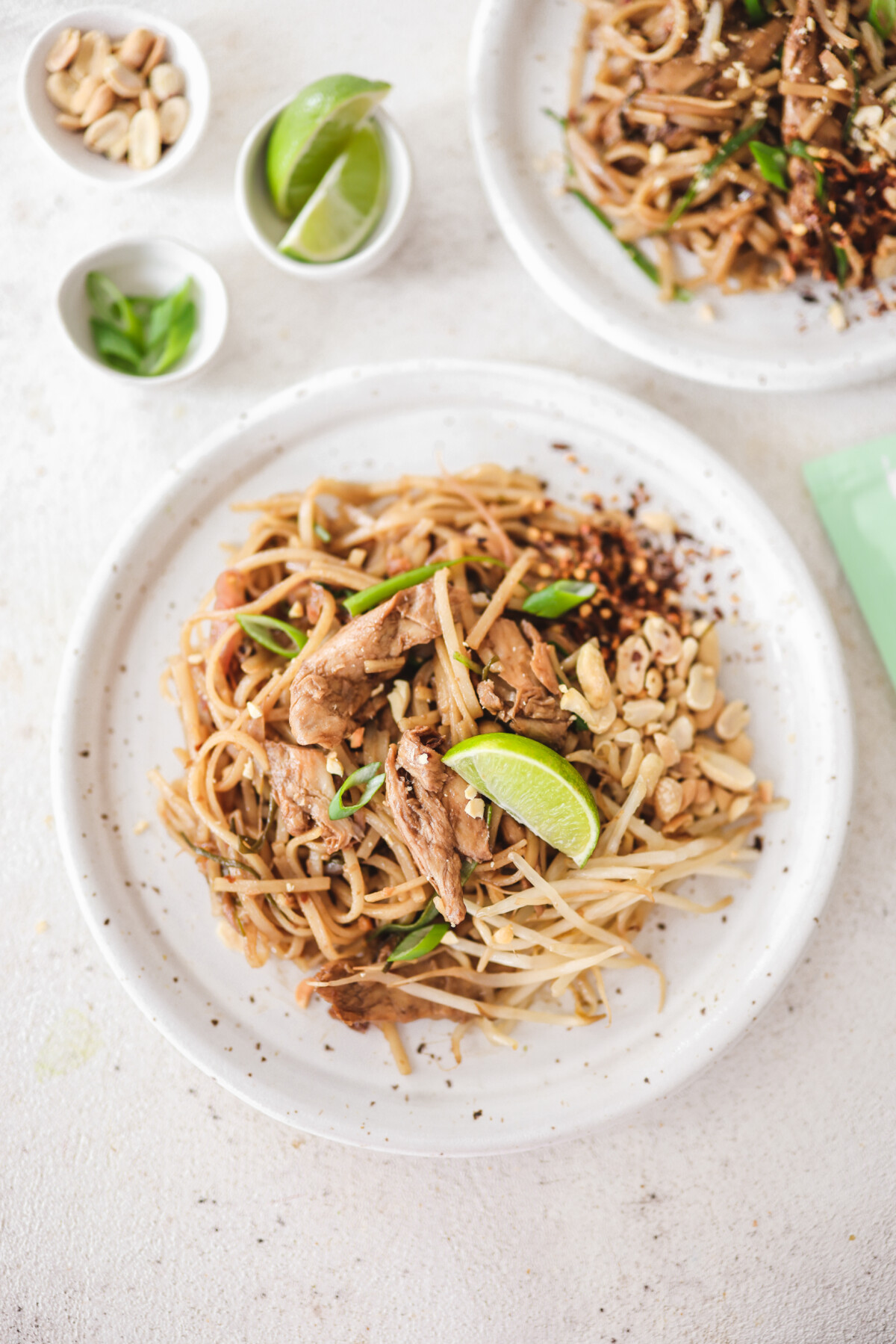 an Asian noodle dish on a white plate topped with peanuts and lime wedges.