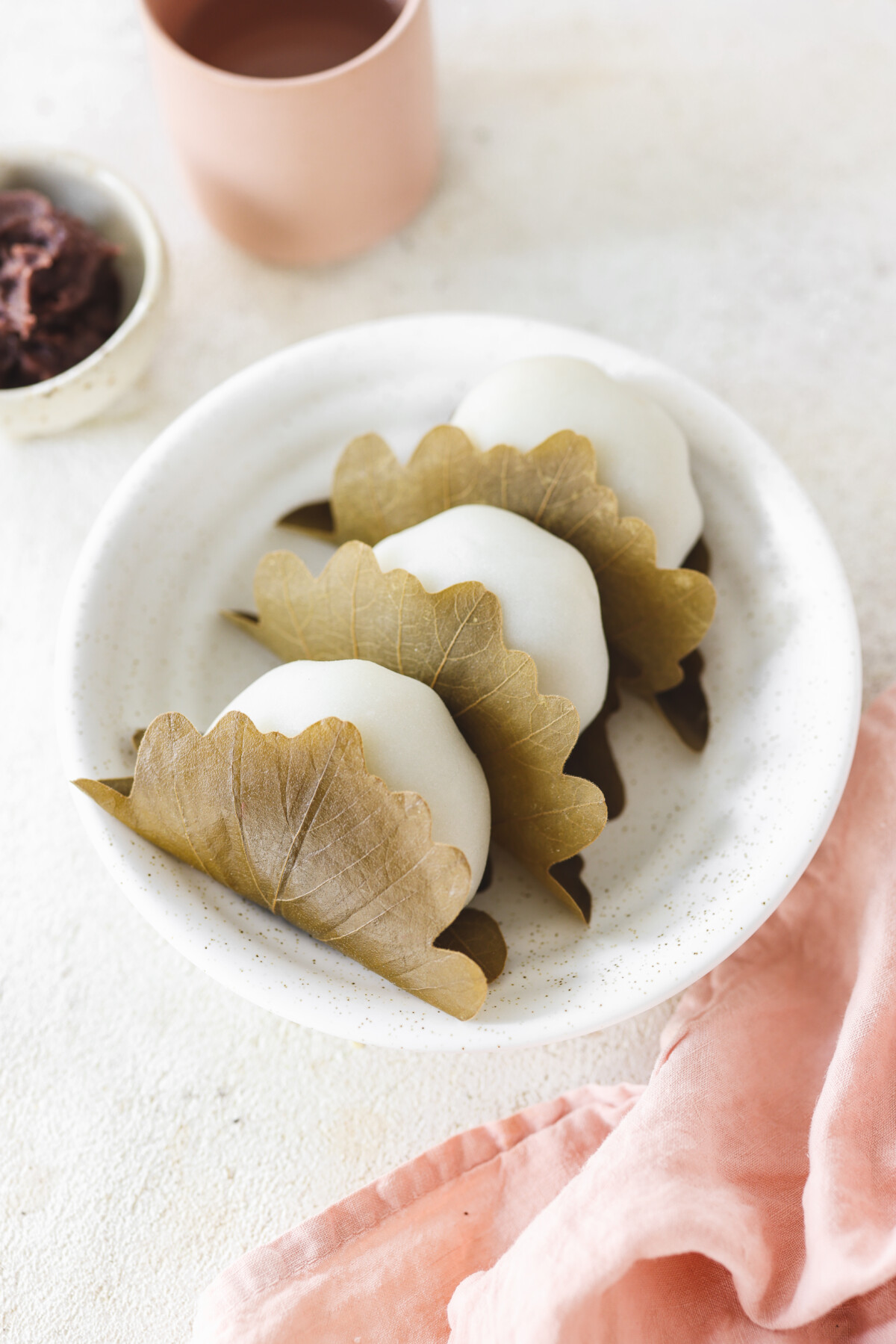 three mochi balls wrapped in oak leaves and on a white plate. 