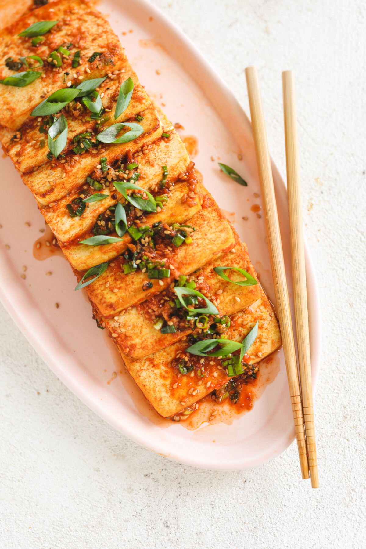 braised tofu on a pink platter topped with scallions and sesame seeds