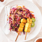 a closeup photo of skewers of tofu next to a cabbage salad