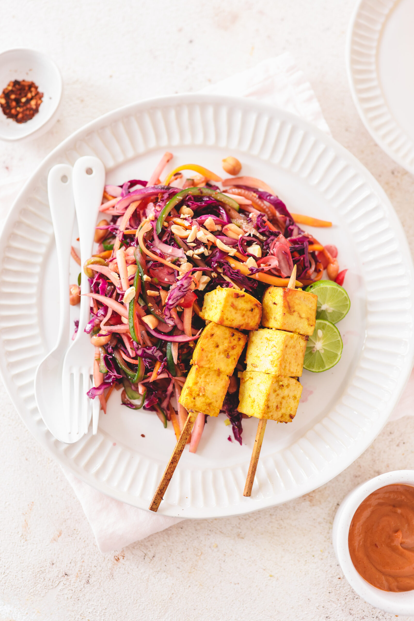 a closeup photo of skewers of tofu next to a cabbage salad