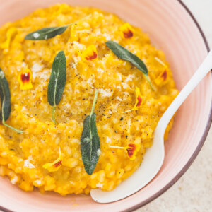 a close up photo of butternut squash risotto in a pink bowl topped with fresh sage