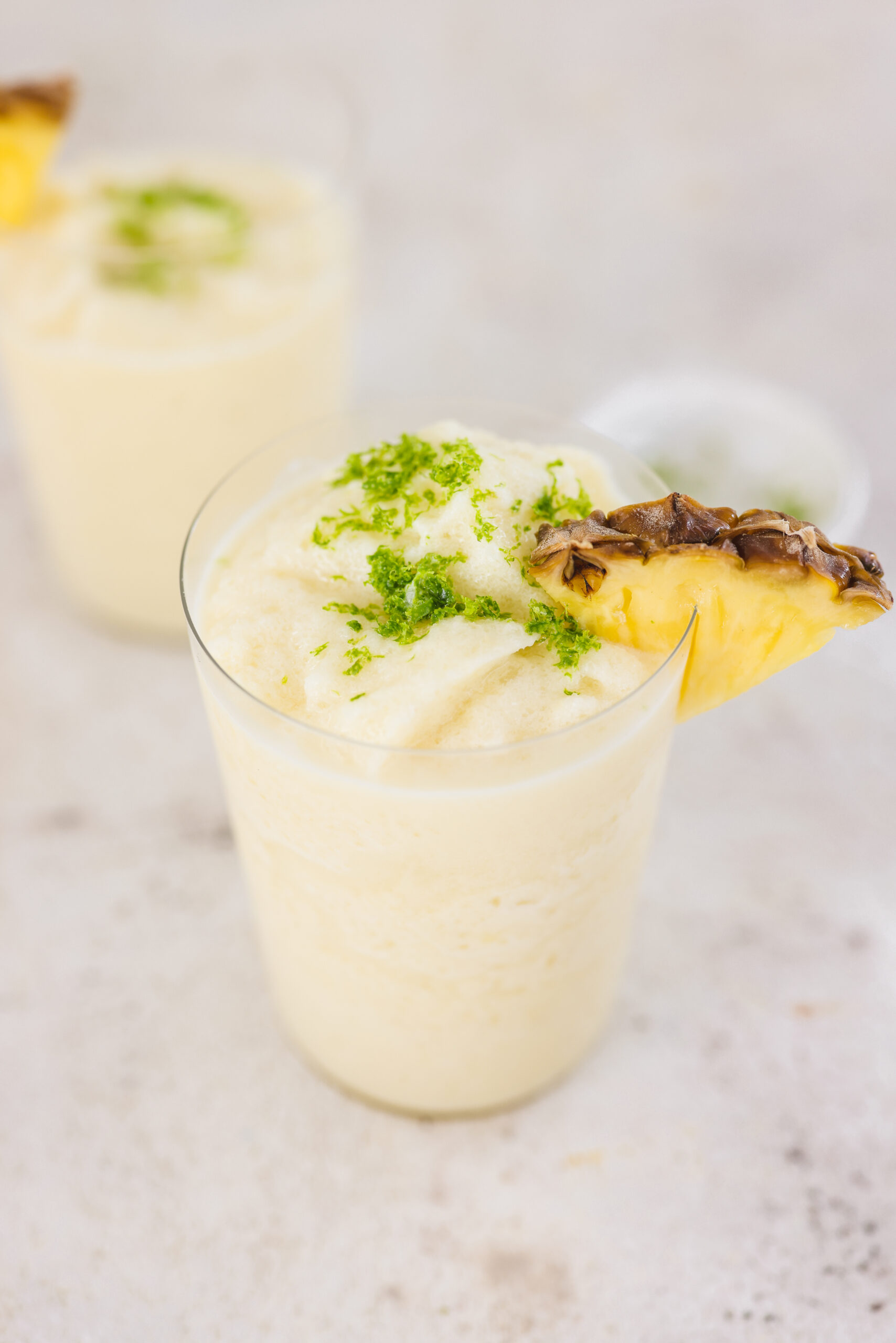 a closeup shot of a pina colada mocktail in a glass topped with a pineapple wedge