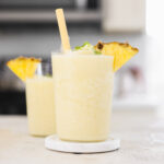 two glasses filled with blended pineapple and coconut cream and garnished with a pineapple wedge.