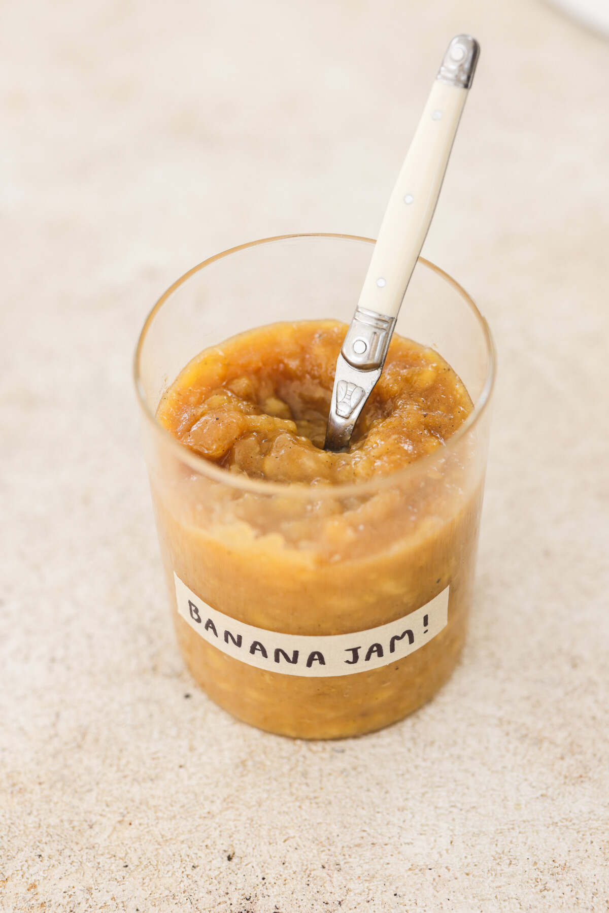 banana jam in a glass jar with a white spoon 