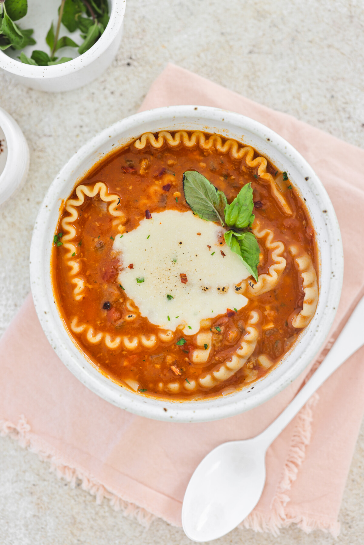 vegan lasagna soup in a white bowl topped with vegan cheese and fresh basil. 
