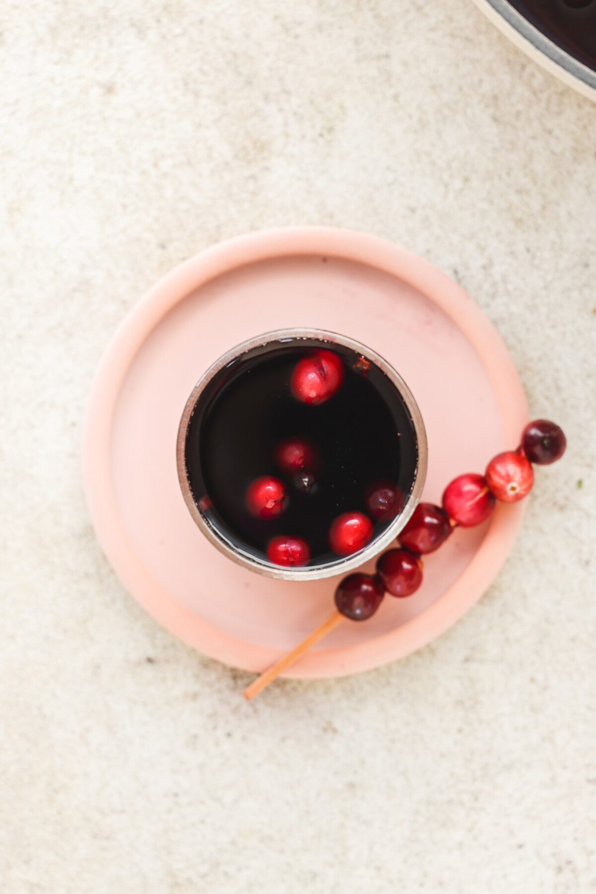 an overhead shot of a glass of non alcoholic mulled wine next to a fresh cranberry skewer. 