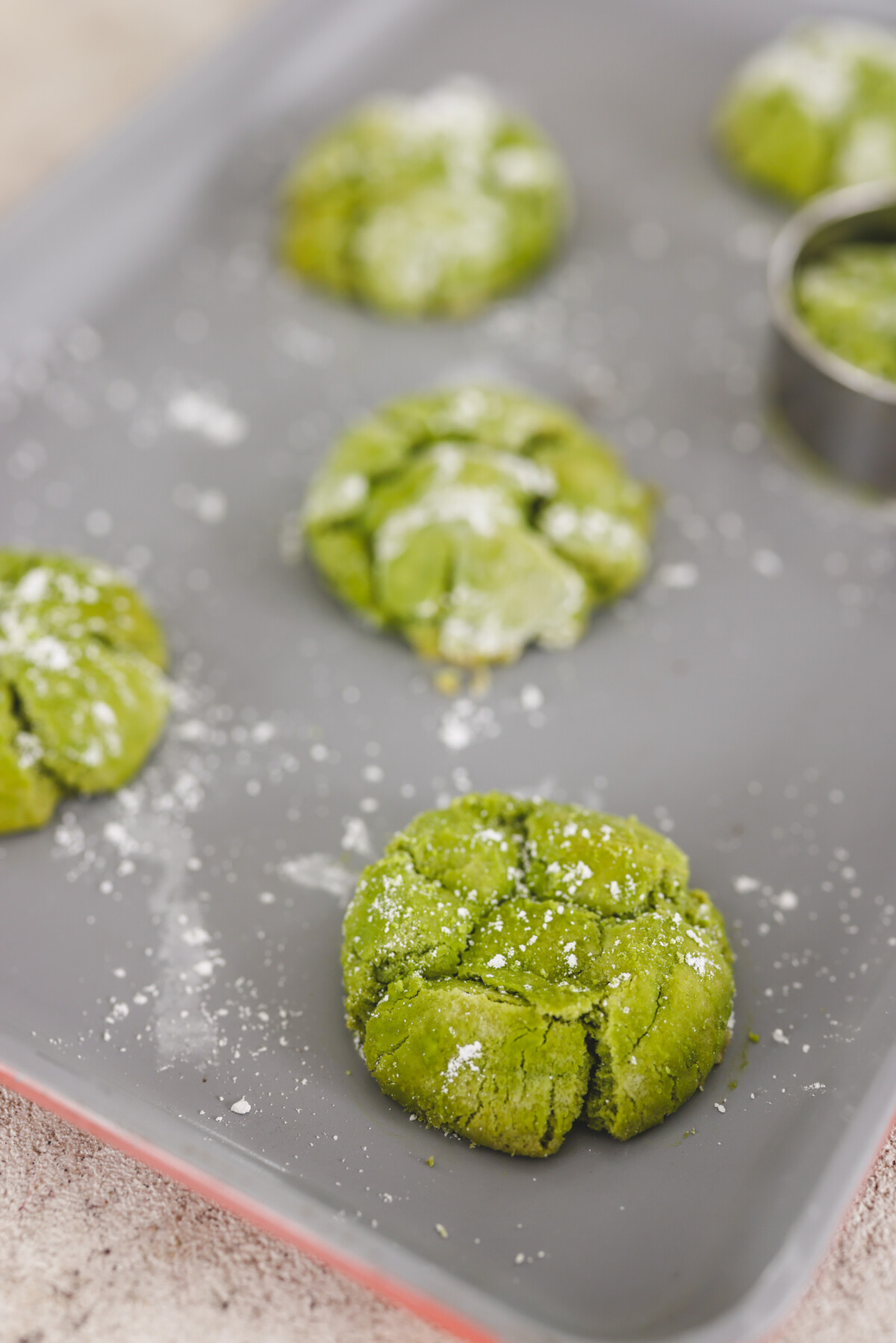 freshly baked matcha crinkle cookies on a silver baking sheet 