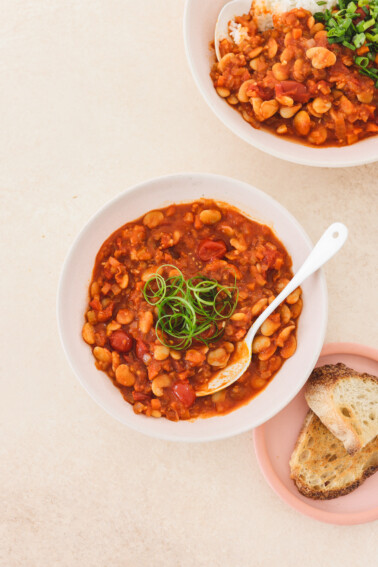 two bowls filled with simmered beans, and a spicy tomato broth.
