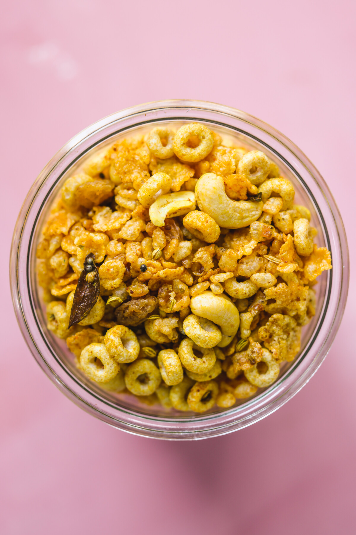 a clear bowl filled with indian snack mix with a pink background